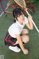 A young woman in a school uniform holding a lacrosse stick.