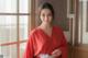 A woman in a red robe standing by a window.