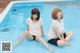 Two young women sitting on the edge of a swimming pool.