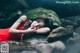 A woman in a red dress laying on a rock in the water.