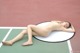 A naked woman laying on a tennis court.