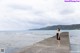 A woman in a black dress standing on a pier by the ocean.